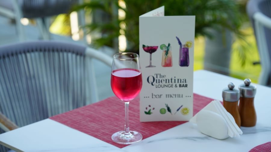 Outdoor dining table with a red drink, condiments and a menu card at Grande Bay Resort & Spa.