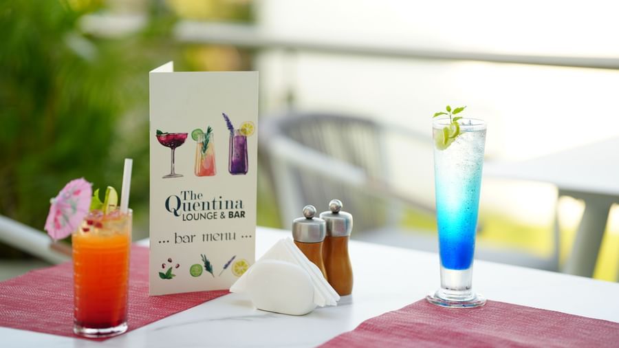 A red and a blue cocktail placed on an outdoor dining table with a menu card at Grande Bay Resort & Spa.