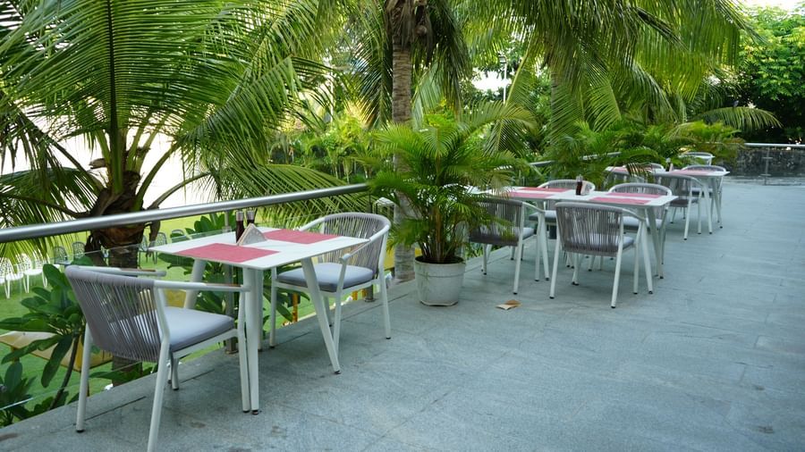 Outdoor dining tables and chairs arranged beside tropical greenery at Grande Bay Resort & Spa.