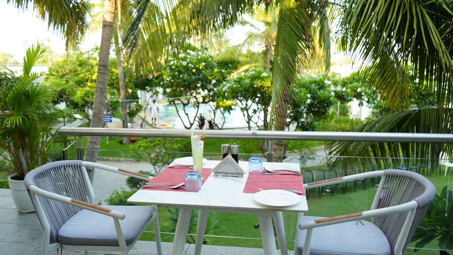 An outdoor dining table with two chairs placed beside palm trees at Grande Bay Resort & Spa.