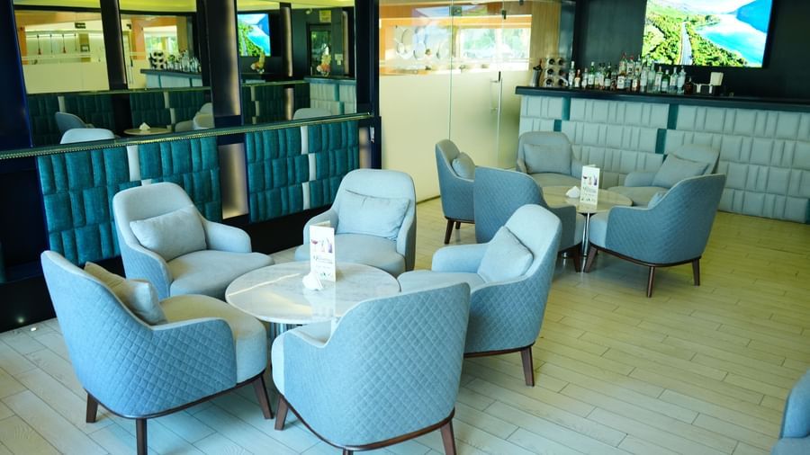 Lounge seating with armchairs and tables beside large glass windows at Grande Bay Resort & Spa.