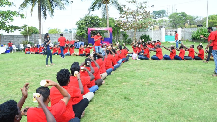 Group of people with red t-shirts seated in a line on a grass in an outdoor lawn with green trees at Grande Bay Resort & Spa.