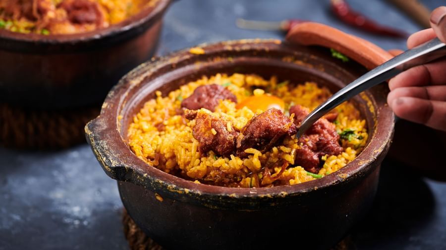 A hand scooping biryani from a clay pot with a spoon at Grande Bay Resort & Spa.