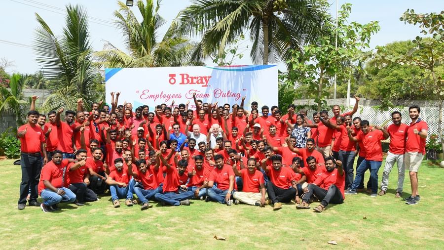 A group of people wearing red t-shirts posing on an outdoor lawn with a banner featuring green trees at Grande Bay Resort & Spa.