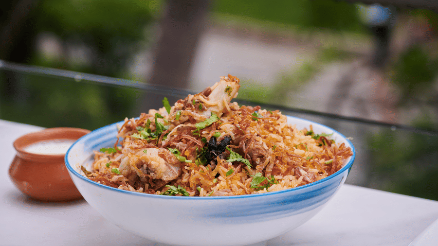 Bowl of biryani served with raita and clay pot on an outdoor table with greenery around - Grande Bay Resort & Spa, Mamallapuram