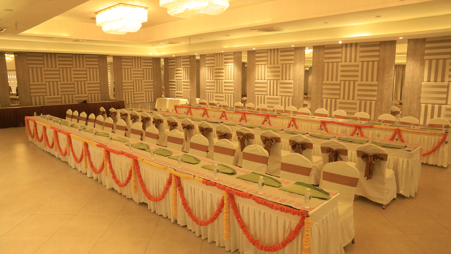 A spacious indoor hall set up with long tables and chairs, adorned with sashes and colourful table runners, ready for a large event or conference - Grande Bay Resort & Spa, Mamallapuram