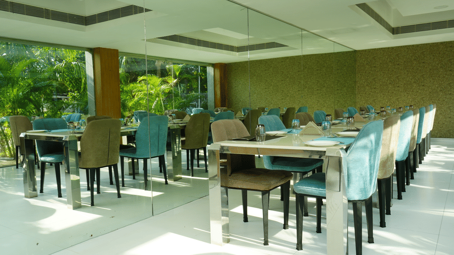 Bright indoor dining section with aligned tables and chairs surrounded by natural light - Grande Bay Resort & Spa, Mamallapuram