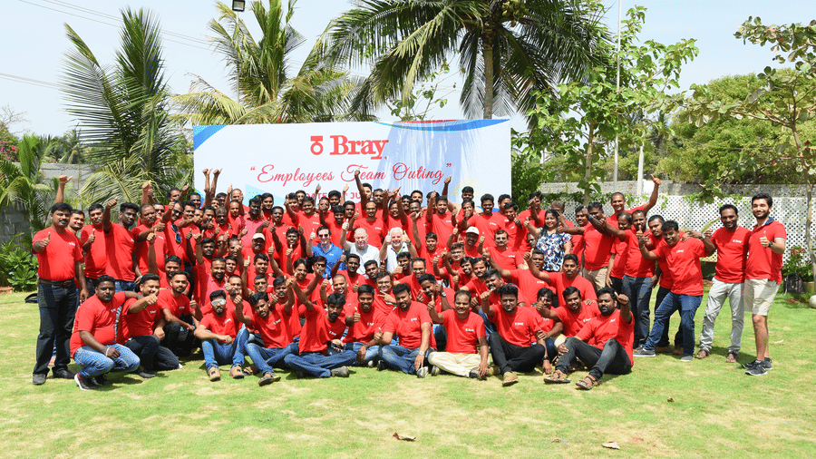 A team outing group in red T-shirts posing on our outdoor lawn with a banner behind them at Grande Bay Resort & Spa, Mamallapuram