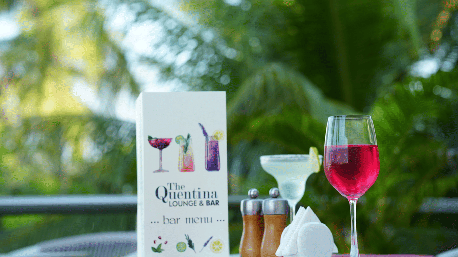 Outdoor table with a menu card, a red drink, a white drink and condiments at Grande Bay Resort & Spa, Mamallapuram.
