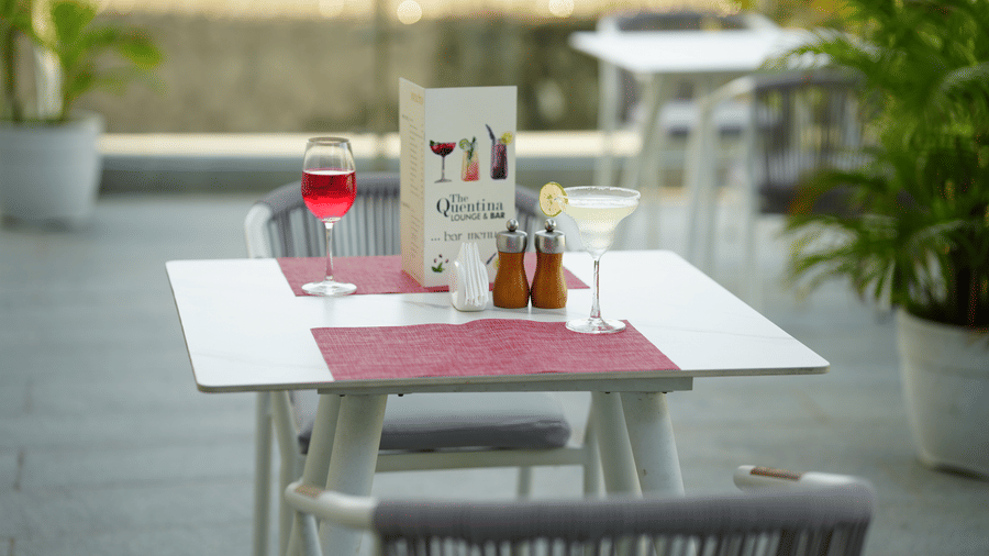 Outdoor table from The Quentina Bar featuring cocktails placed along a tranquil garden walkway - Grande Bay Resort & Spa, Mamallapuram