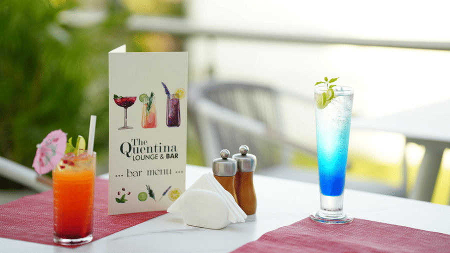 Colourful beverages arranged on an outdoor table from The Quentina Bar with lush garden scenery - Grande Bay Resort & Spa, Mamallapuram