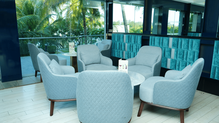 Cosy seating clusters inside The Quentina Bar featuring plush grey chairs and coconut tree views through large windows - Grande Bay Resort & Spa, Mamallapuram