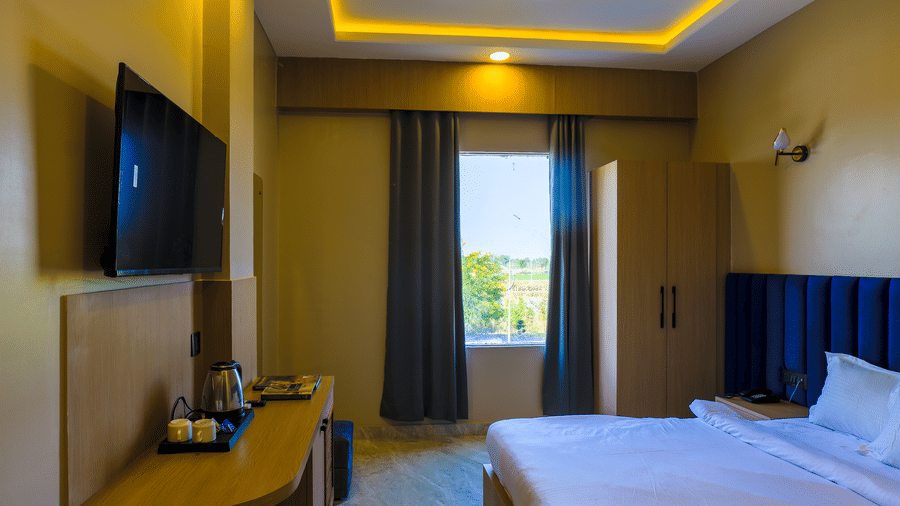 A room at Grassfield Riviera Resort, with a large bed, linens, wood furniture, and a television, a wall mounted air-conditioner.