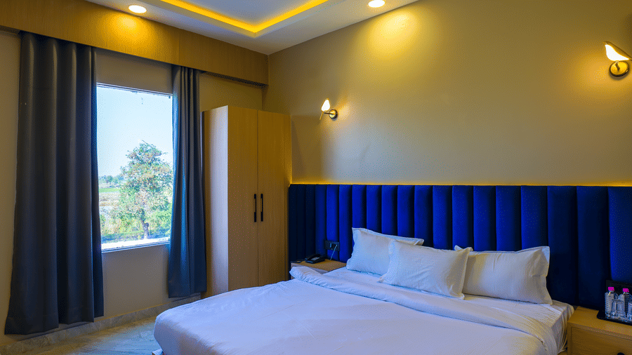 A room with a large bed, a headboard, a window with curtains, and warm lighting.