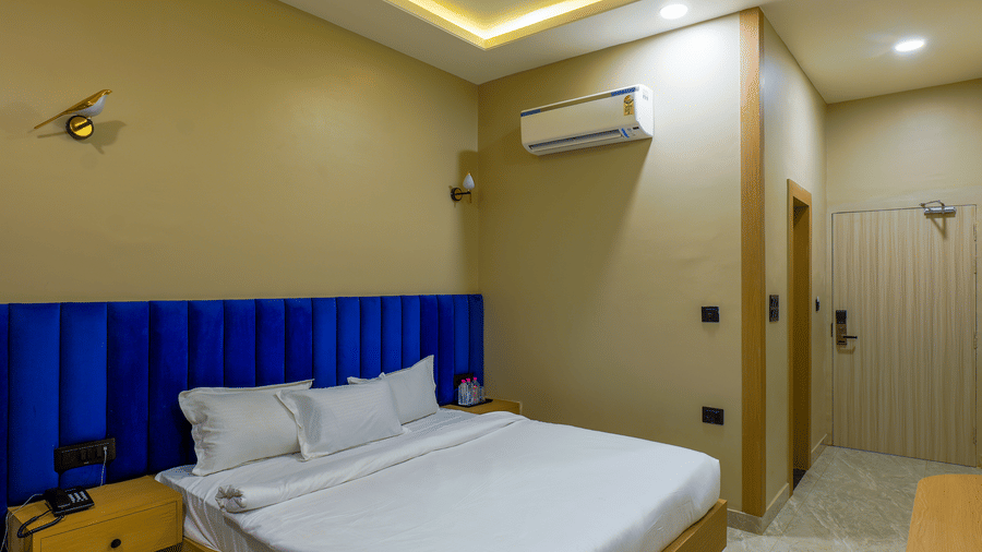 A room at Grassfield Riviera Resort, with a large bed, headboard, linens, wood furniture, and a wall mounted air-conditioner.