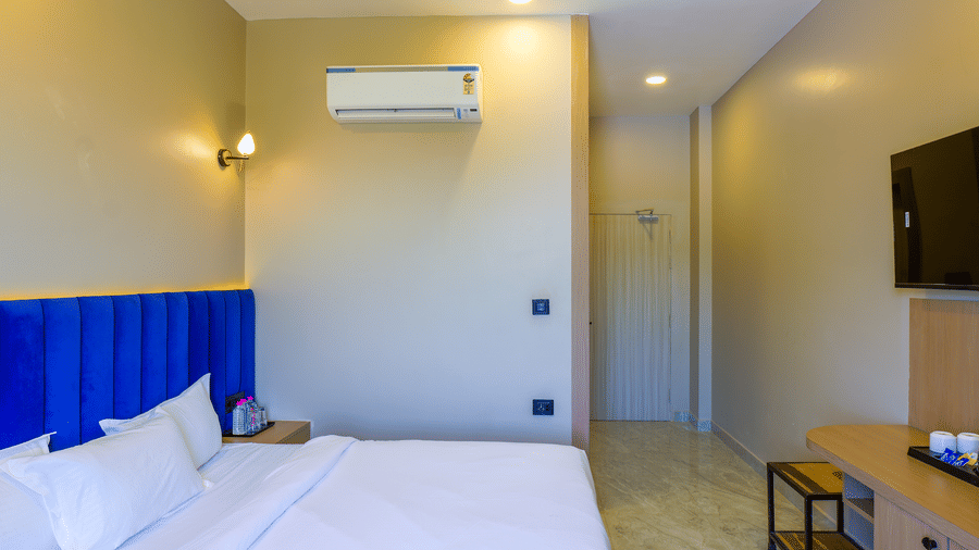 A room with a large bed, a headboard, wood walls, a television, a table, a wall mounted air-conditioner, and furniture.