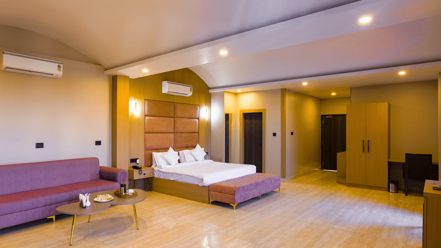 A wide view of the Suite showcasing a double bed, a large sofa, warmly-lit ceiling lights, and wooden flooring atGrassfielld Riveria Resort.