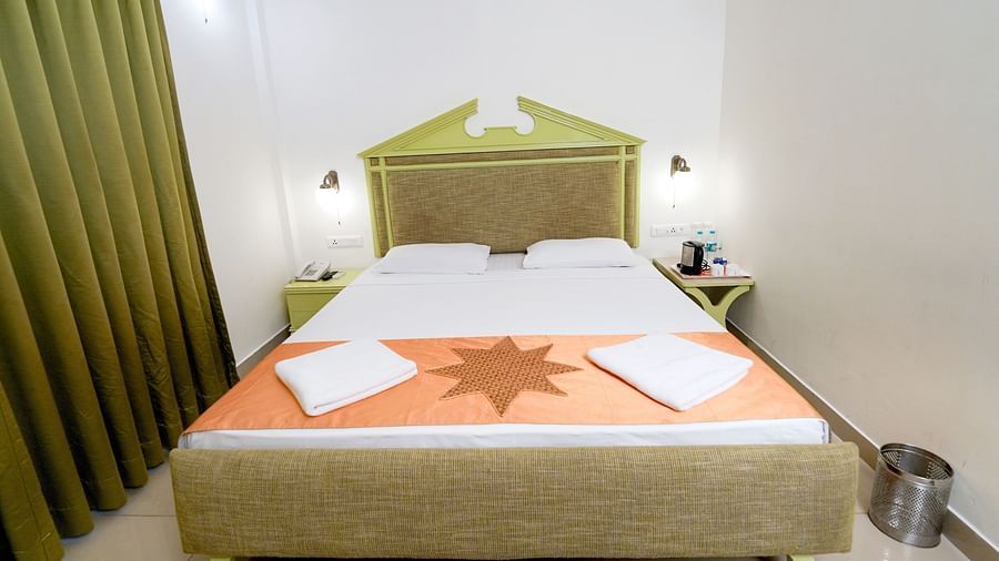 A hotel bedroom with a large double bed, green headboard, and curtains, with warm lighting at Greens Inn - Luxury Rooms in Ramoji Film City.