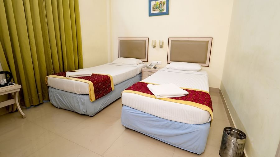 Another twin bedroom with white bedding, a mustard runner, air conditioning, and a green curtain at Greens Inn - Comfortable Stay in Ramoji Film City.