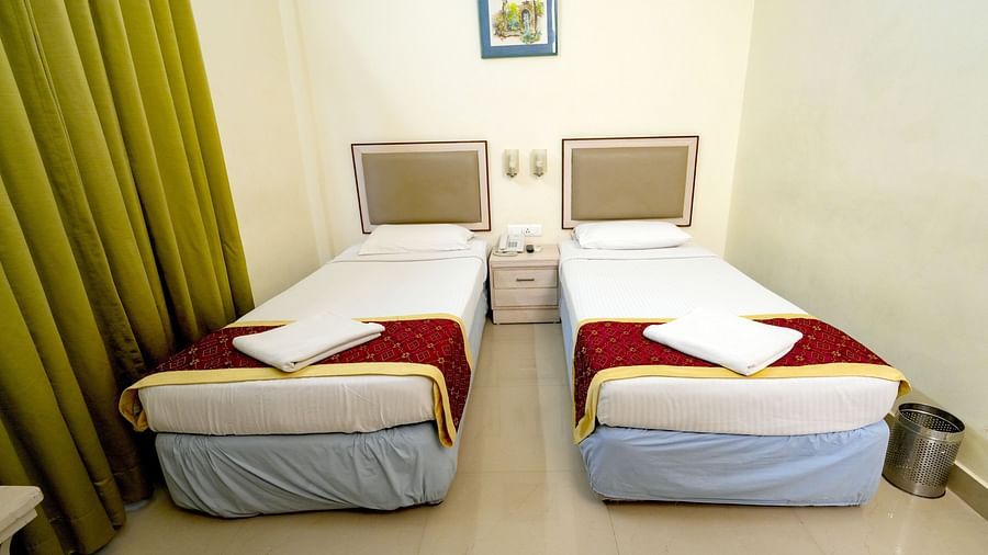 A hotel twin bedroom with white and mustard bedding, green curtains, and a picture on the wall at Greens Inn - Comfortable Twin Rooms in Ramoji Film City.