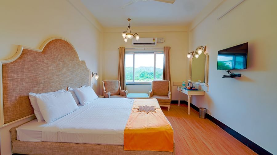 A well-appointed hotel room with a large bed, orange throw, wooden flooring, and a TV. - Greens Inn - Cozy Accommodations