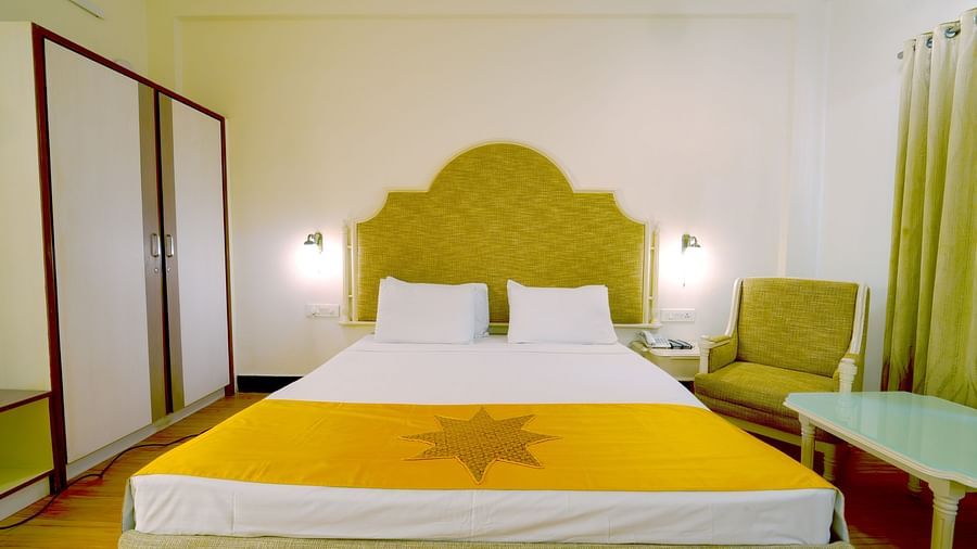 A spacious hotel room with a large double bed with a yellow cover, green headboard, and a sitting area at Greens Inn - Spacious Rooms in Ramoji Film City.