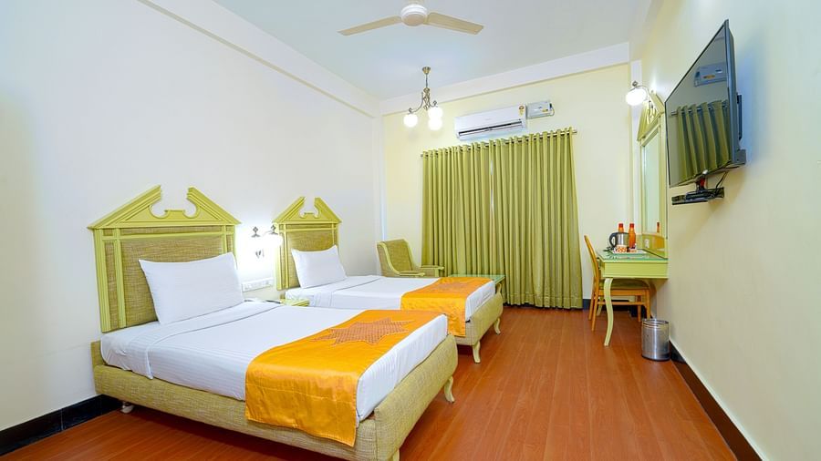 A twin hotel room with light wooden flooring, green headboard, and mustard accents, offering a cozy atmosphere at Greens Inn - Cozy Twin Rooms in Ramoji Film City.