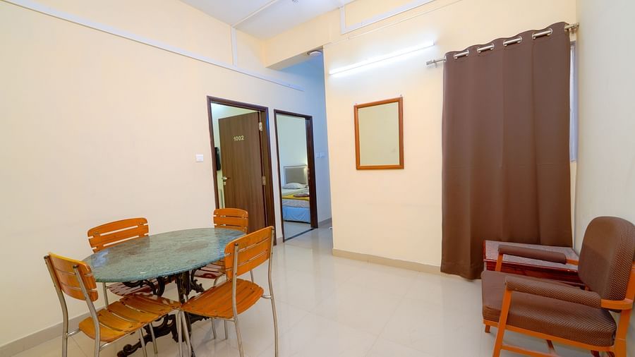 A modest hotel room with a glass table, chairs, and an armchair, complemented by brown drapes at Greens Inn - Affordable Hotel Rooms in Ramoji Film City.