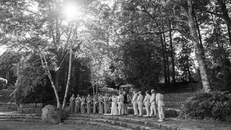 Wedding ceremony at Hartstone Inn with the couple, officiant, bridesmaids, and groomsmen standing on stone steps surrounded by trees and sunlight filtering through.