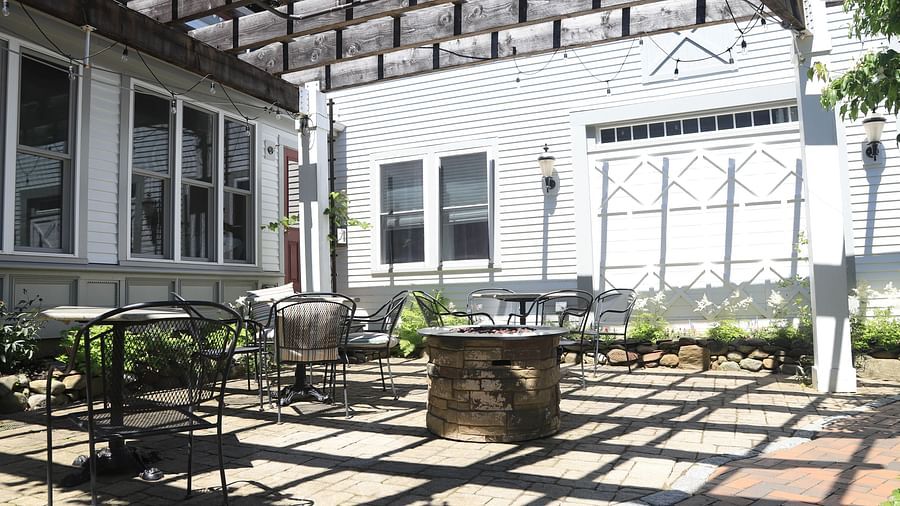 Outdoor sunny courtyard with pergola, wood furniture, and brick flooring at Hartstone Inn