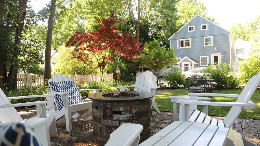 Outdoor garden seating area with white Adirondack chairs and a view of Hartstone Inn in the background.