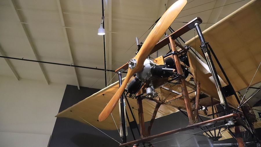 Close-up of a vintage wooden biplane suspended from the ceiling at Hartstone Inn’s aviation-themed exhibit, showcasing its large wooden propeller, radial engine, and fabric-covered wings under overhead lighting