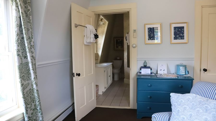 Cozy room with blue table and showing the bathroom from far with vanity sink and towel hanging  at Hartstone Inn.