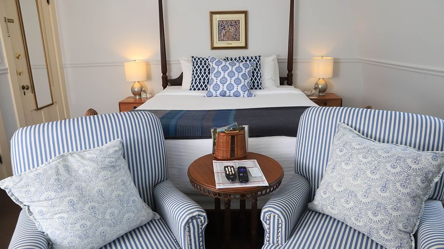 Seating area with striped chairs, tray table and showcasing a king size bed in the background at Hartstone Inn