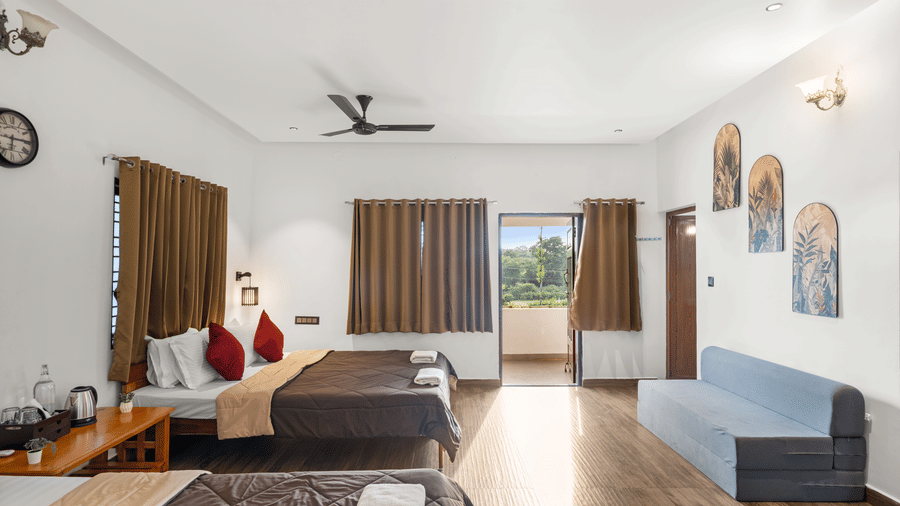 Room at Hatti Eden Coorg offering a comfortable bed, sofa, balcony access, modern furnishings, air conditioning and scenic outdoor views for a peaceful stay in Coorg.