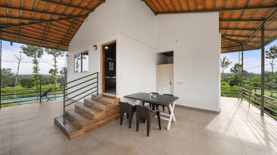 Covered balcony with outdoor table and chairs overlooking lush greenery at Hatti Eden Coorg.