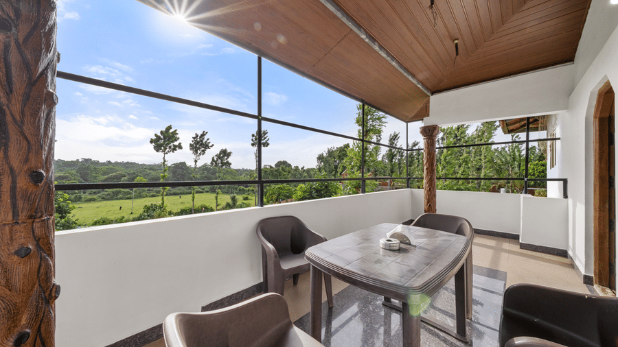 Covered balcony with outdoor table and chairs overlooking lush greenery at Hatti Eden Coorg.