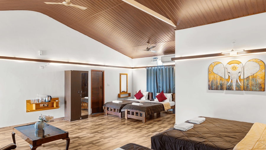 Bedroom with beds dressed in brown linen and red cushions, wall art, wooden furniture and a panelled wooden ceiling throughout the room.