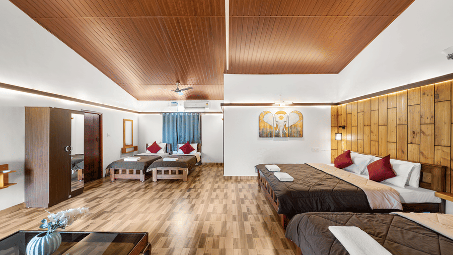Open living area with beds dressed in brown linen, wooden furniture, blue accent decor and a panelled wooden ceiling throughout the room.