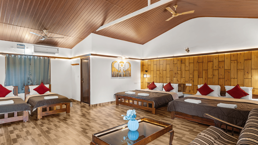 Open living area with sofas and beds dressed in brown linen and red cushions, wooden furniture and a panelled wooden ceiling overhead.