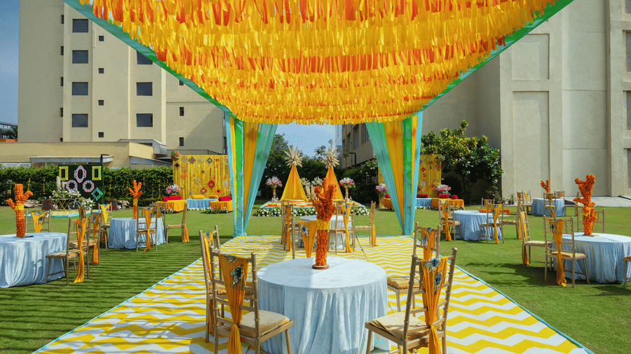 2 tables with chairs in a cluster seated underneath a canopy during a sunny afternoon for shade - The Hideaway Banquets & Lawns, Greater Noida