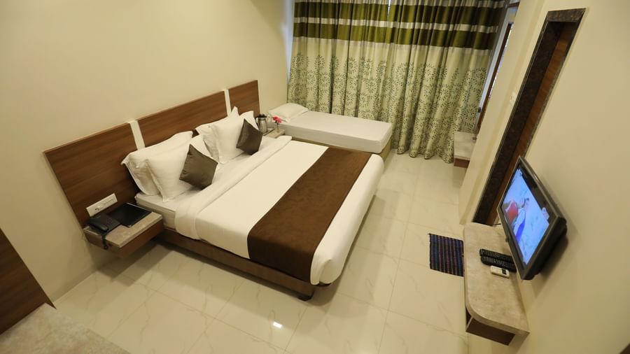 Extended view of the queen size bed and single bed facing the wall-mounted TV in the Deluxe Room of Highland Resort.