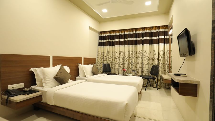 A Super Deluxe Room of Highland Resort furnished with twin beds, a wall-mounted TV, seating area for two, and closed curtains.