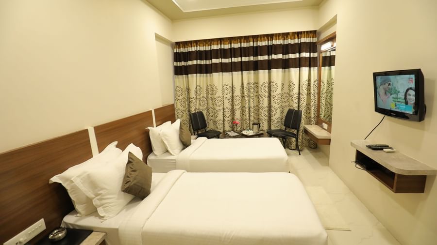 Side view of the Super Deluxe Rooms, of Highland Resort, that are furnished with twin beds, wall-mounted TV, a seating area for two, and drawn curtains.