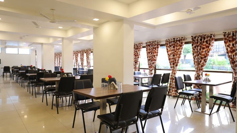 Dining tables in the spacious Darbar Restaurant that has glass windows through which natural light seeps in, at Highland Resort.