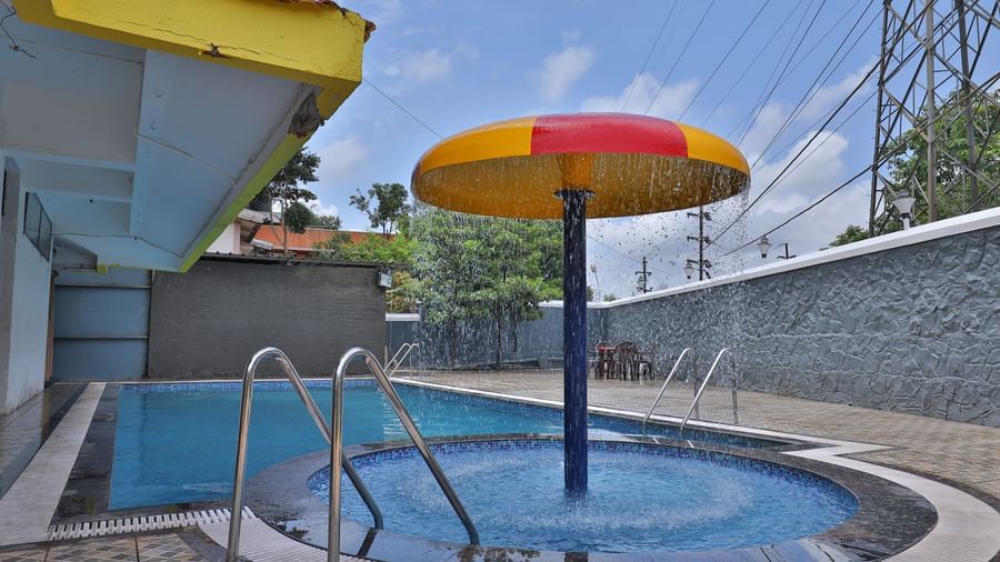 Outdoor swimming pool area with a separate circular kids’ pool featuring a mushroom-shaped water feature, pool ladders, tiled flooring at Highland Resort.