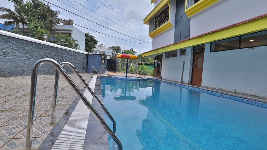 Outdoor swimming pool area with a separate circular kids’ pool featuring a mushroom-shaped water feature, pool ladders, tiled flooring at Highland Resort.