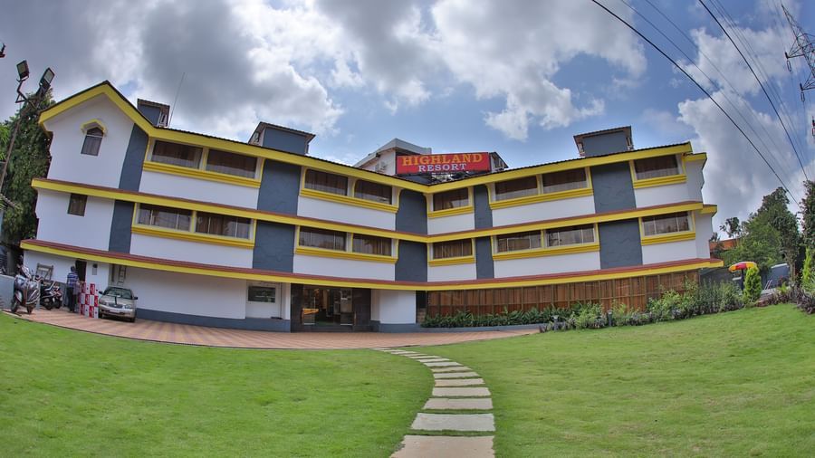 A stone pathway on a grass lawn, leading to the multi-storey Highland Resort which has a large signboard on top.