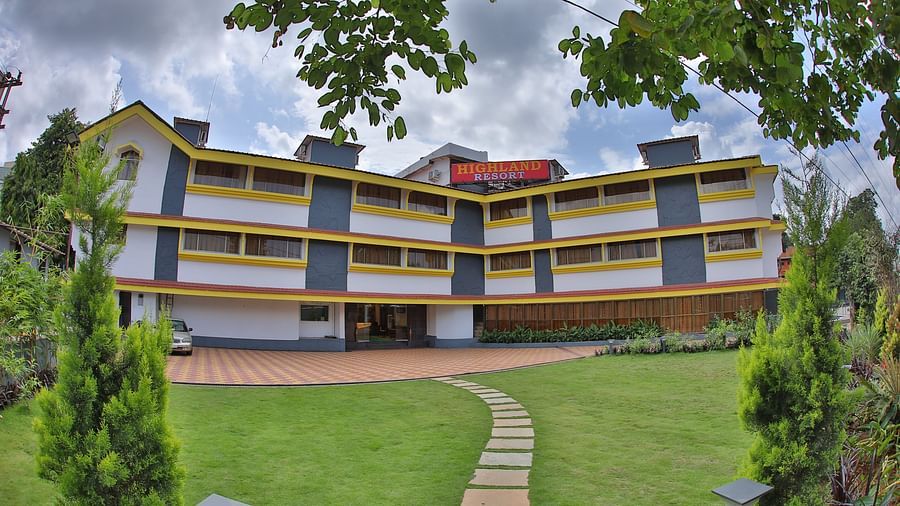 A stone pathway on a grass lawn, leading to the multi-storey Highland Resort which has a large signboard on top.