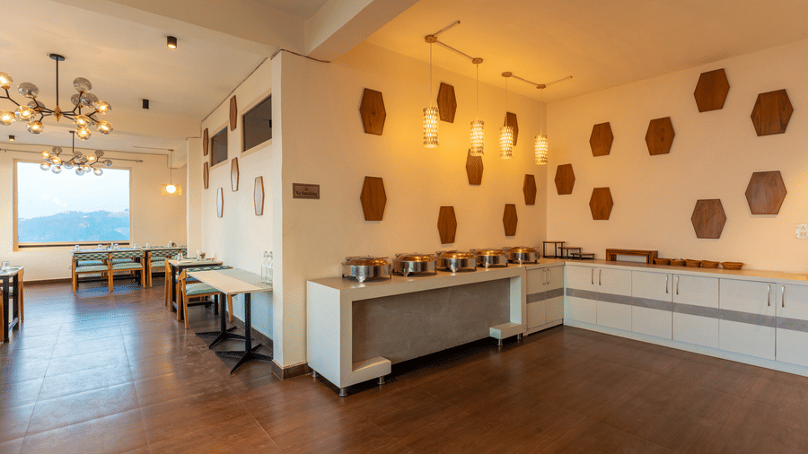 A long shot of the wide and brightly lit dining hall featuring unique geometric wall art at Himalayas Resort By The Lake Hill, Mukteshwar.